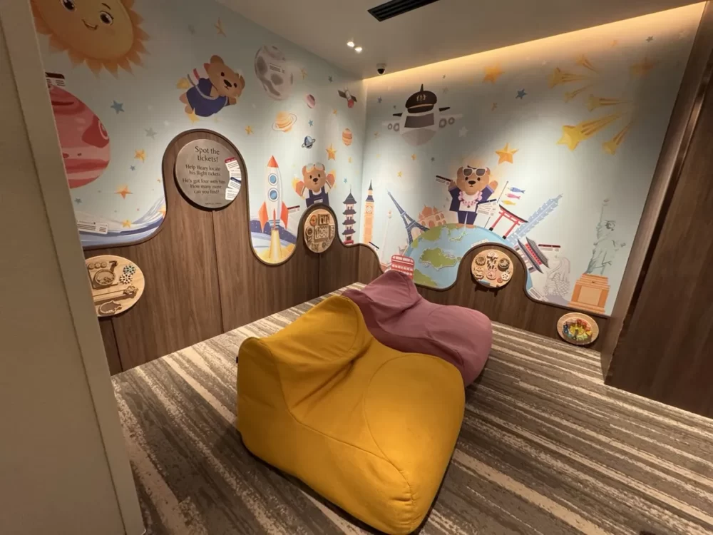 キッズプレイルーム内部。旅するクマの壁画、仕掛けパネル、黄色と紫のビーズソファ