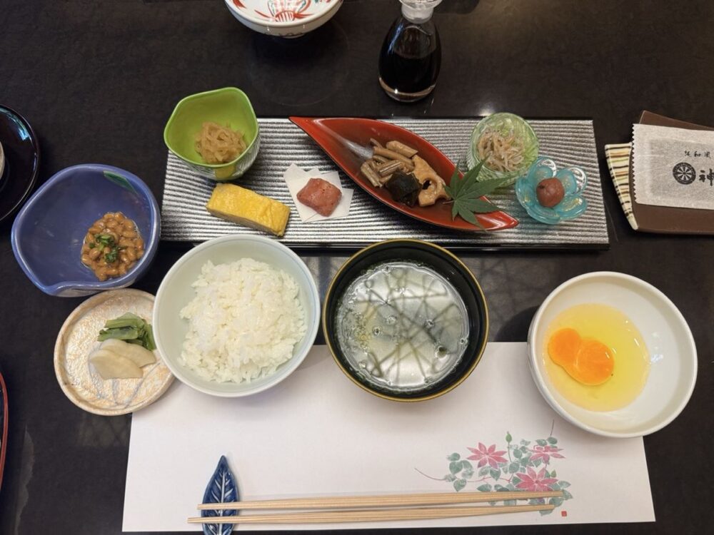 旅館 神仙の朝食一式。ご飯、汁物、卵かけご飯用の生卵、小鉢が並ぶ